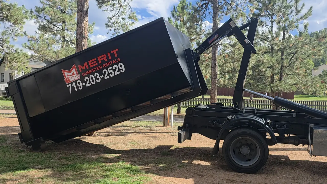 A Merit hooklift truck setting a roll-off container down on a driveway