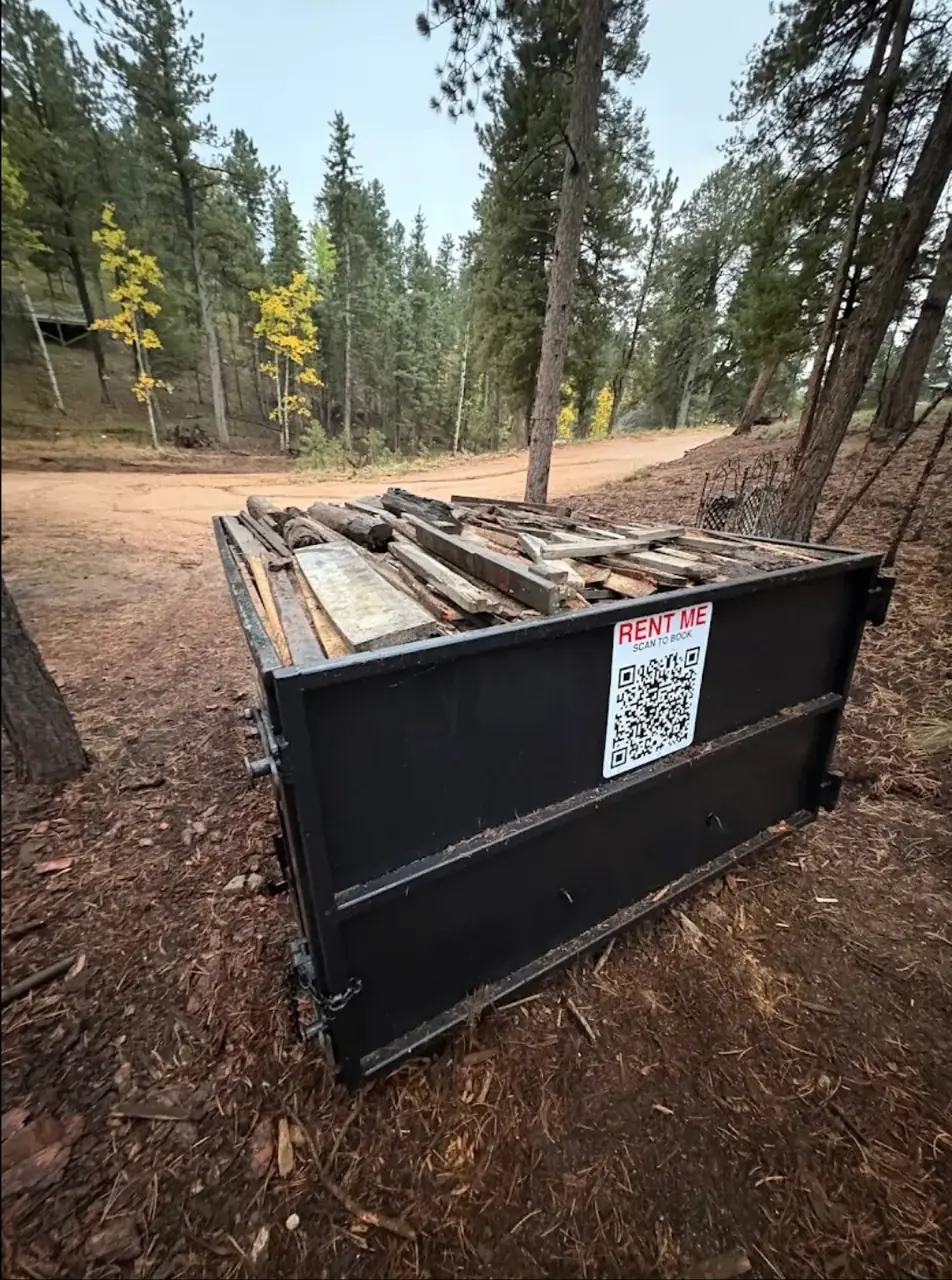 A Merit container loaded level with the rail with old lumber and decking on a mountain lot